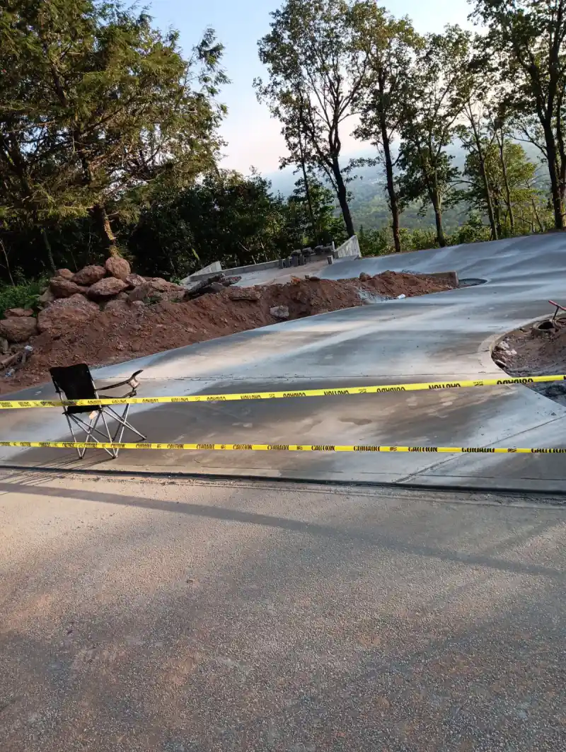 A wide concrete driveway on high ground with a distant valley and tree line beyond, caution tape strung across the fresh slab.