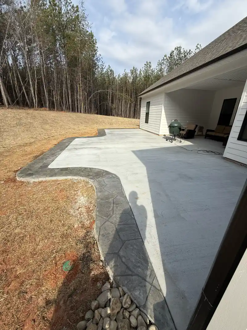 A concrete patio with a stamped decorative border framing a broom-finished central field.